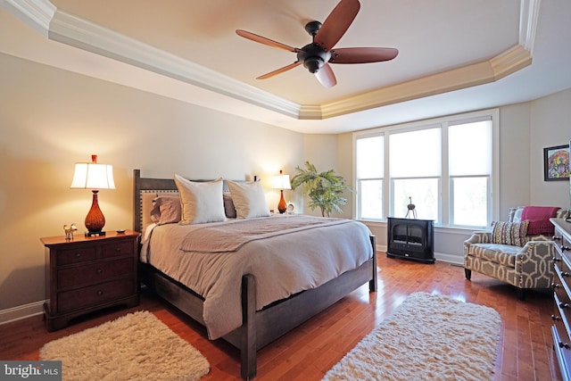 bedroom featuring hardwood / wood-style flooring, baseboards, a raised ceiling, and crown molding