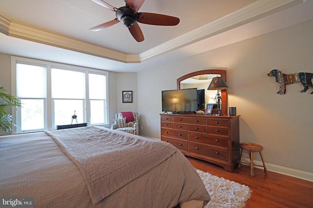 bedroom with baseboards, a raised ceiling, ceiling fan, wood finished floors, and crown molding