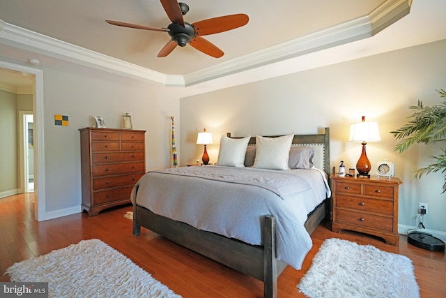 bedroom with wood finished floors, a ceiling fan, baseboards, ornamental molding, and a tray ceiling