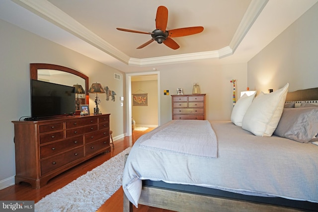 bedroom with ornamental molding, a tray ceiling, baseboards, and wood finished floors