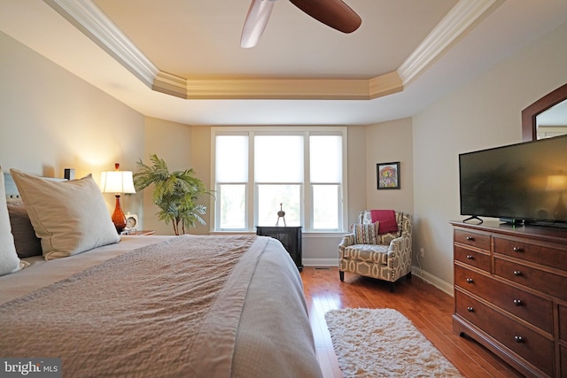 bedroom with ornamental molding, a tray ceiling, baseboards, and wood finished floors