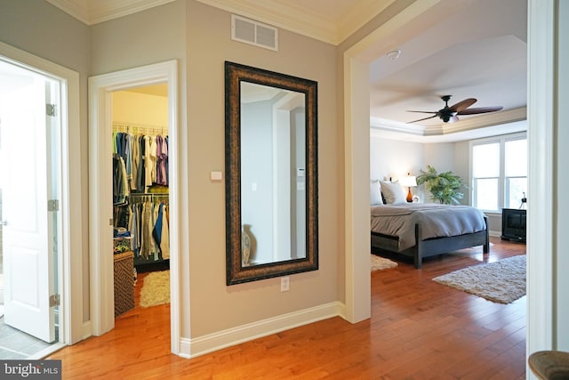 hallway featuring a tray ceiling, visible vents, ornamental molding, light wood-type flooring, and baseboards