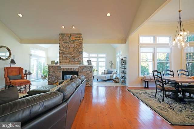 living area featuring high vaulted ceiling, light wood-style flooring, a notable chandelier, a fireplace, and baseboards