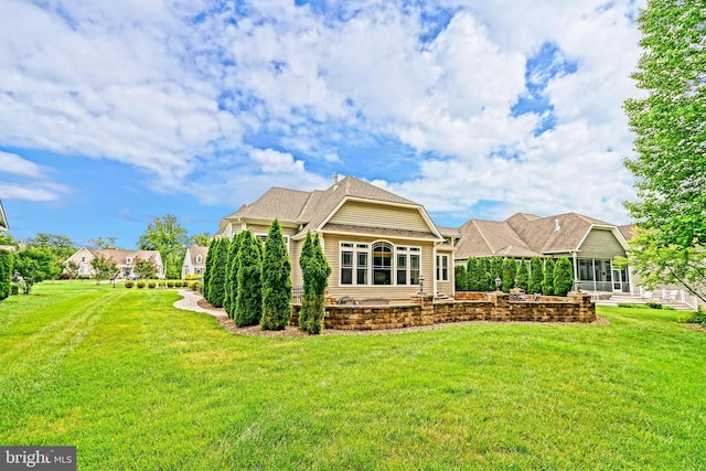 rear view of property with a sunroom, roof with shingles, and a yard