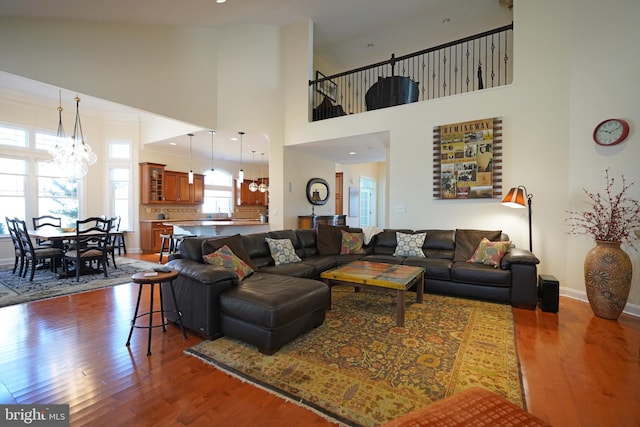 living area featuring dark wood-style flooring, a notable chandelier, a towering ceiling, ornamental molding, and baseboards