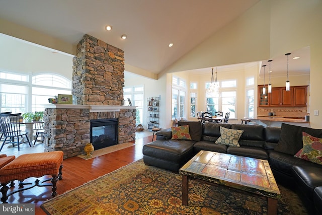 living area with plenty of natural light, high vaulted ceiling, wood finished floors, and a stone fireplace