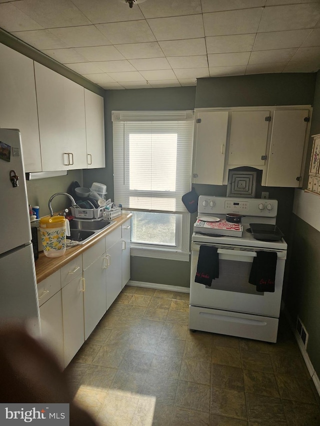 kitchen featuring white range with electric cooktop, visible vents, freestanding refrigerator, white cabinets, and a sink