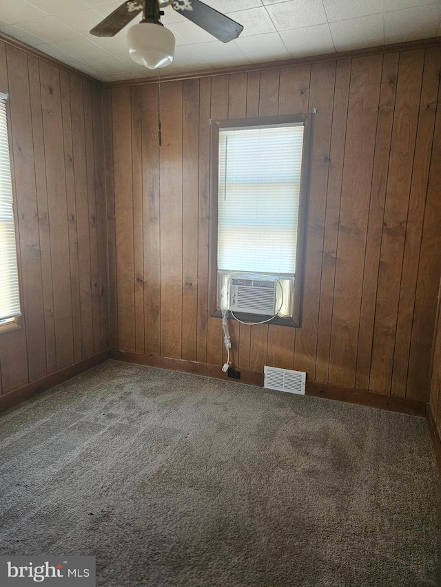 carpeted spare room featuring visible vents, baseboards, ceiling fan, cooling unit, and wood walls