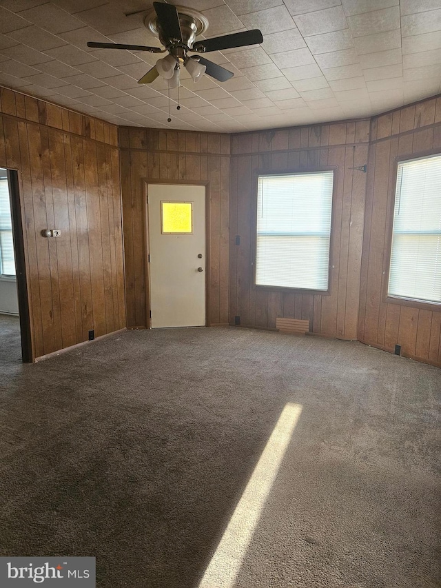 empty room featuring ceiling fan, wood walls, and carpet flooring