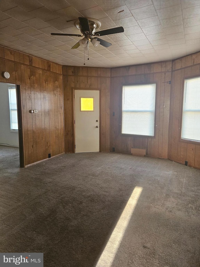 carpeted empty room with a ceiling fan and wooden walls