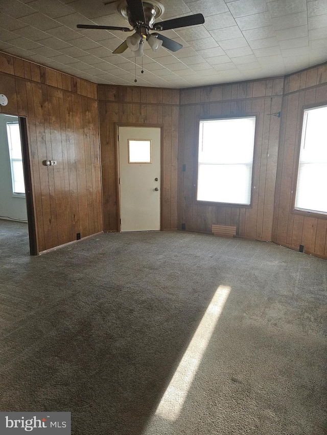 carpeted empty room with wood walls and a ceiling fan