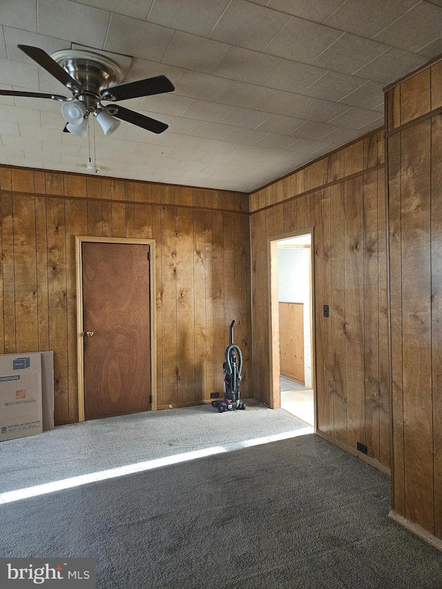 empty room with carpet floors, wood walls, and a ceiling fan