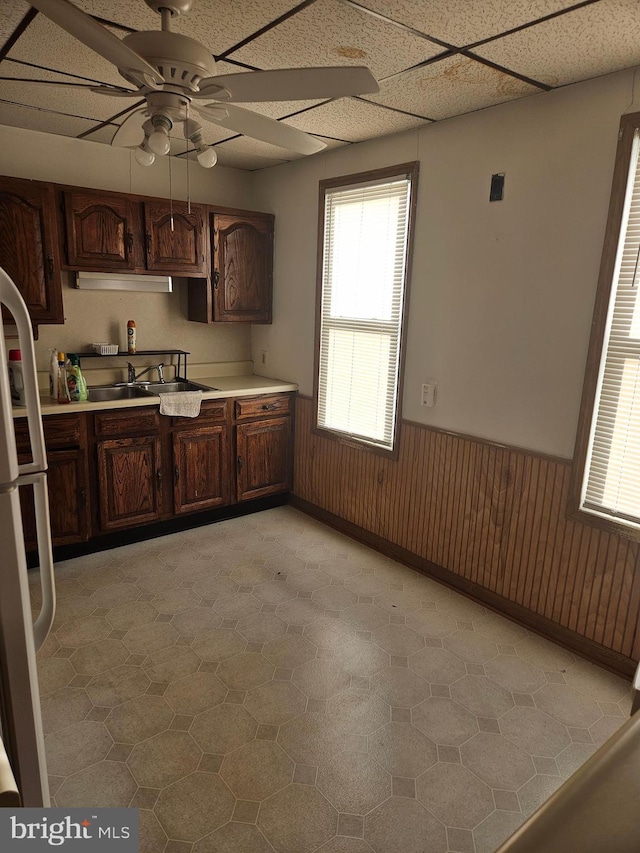 kitchen featuring light countertops, freestanding refrigerator, wainscoting, a sink, and wooden walls