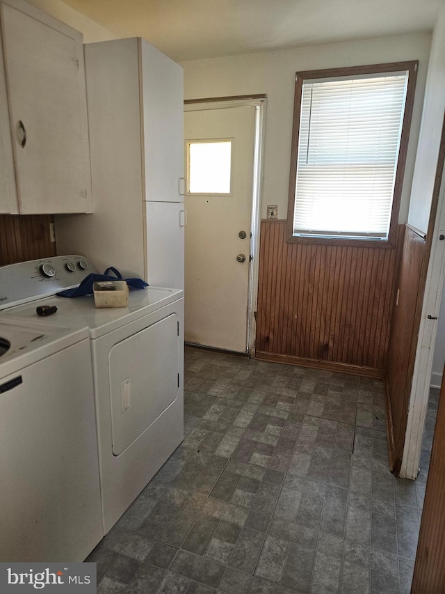 laundry room featuring a wainscoted wall, washer and clothes dryer, cabinet space, wooden walls, and plenty of natural light