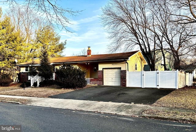 ranch-style home with driveway, a chimney, an attached garage, a gate, and brick siding