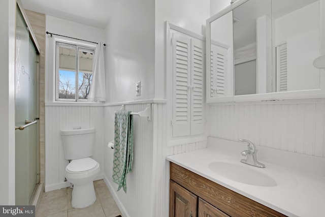 bathroom featuring tile patterned flooring, toilet, a wainscoted wall, vanity, and an enclosed shower