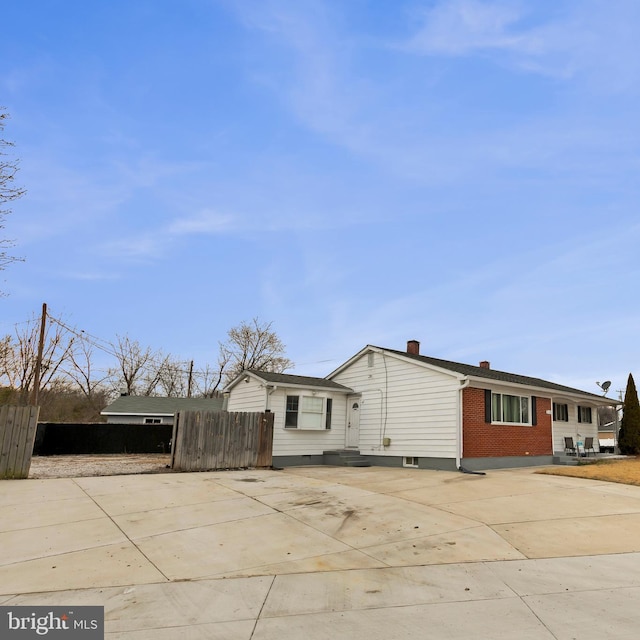 view of front of property featuring driveway, a chimney, fence, and brick siding