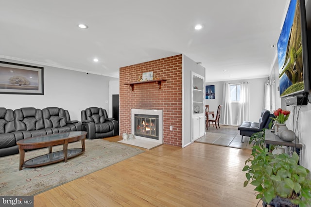 living room featuring a brick fireplace, crown molding, wood finished floors, and recessed lighting