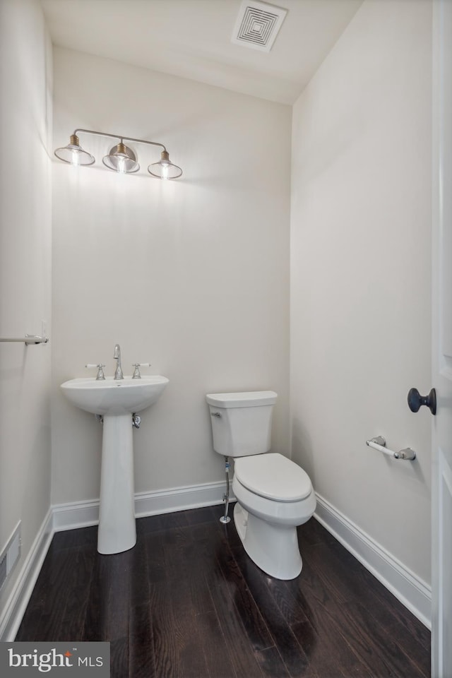 half bathroom featuring toilet, baseboards, visible vents, and wood finished floors