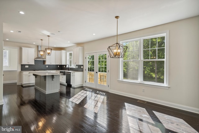 kitchen featuring tasteful backsplash, wall chimney range hood, white cabinets, and baseboards