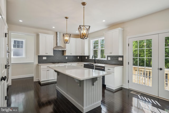 kitchen with light countertops, wall chimney range hood, gas cooktop, and white cabinets