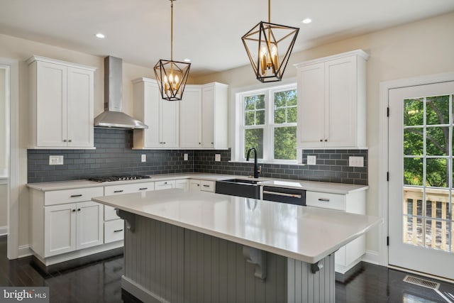 kitchen with a sink, visible vents, light countertops, dishwasher, and wall chimney exhaust hood