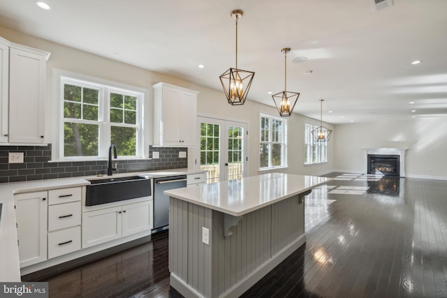 kitchen with dark wood-type flooring, a sink, decorative backsplash, dishwasher, and a glass covered fireplace