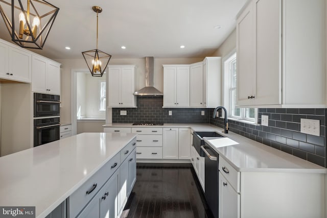 kitchen featuring light countertops, stainless steel dishwasher, a sink, gas cooktop, and wall chimney exhaust hood