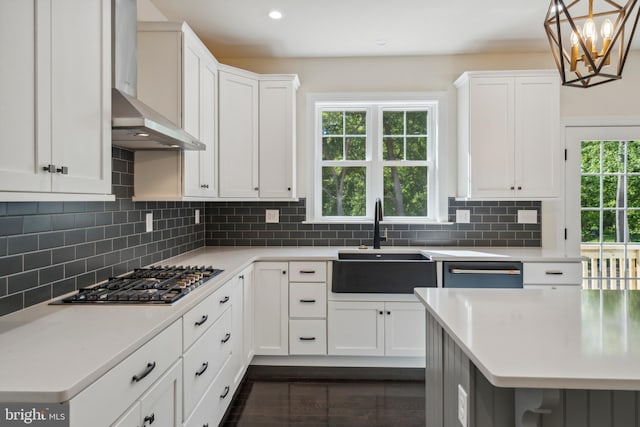 kitchen with tasteful backsplash, light countertops, stainless steel gas stovetop, a sink, and wall chimney exhaust hood