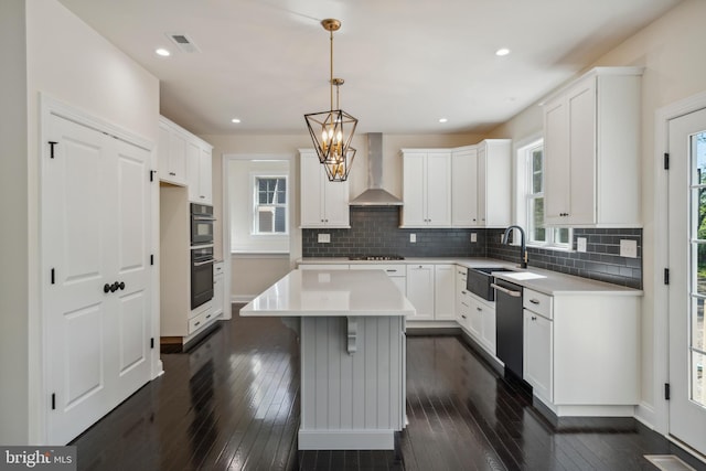 kitchen with dark wood-type flooring, gas stovetop, a sink, wall chimney range hood, and stainless steel dishwasher