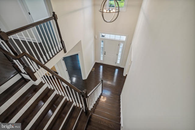 foyer with baseboards, wood-type flooring, a high ceiling, stairs, and a notable chandelier