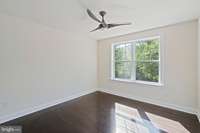 empty room with dark wood-type flooring, visible vents, ceiling fan, and baseboards