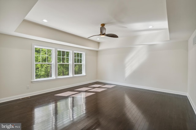 empty room with a tray ceiling, wood-type flooring, visible vents, and baseboards