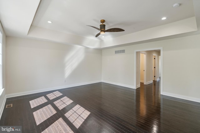 spare room featuring a tray ceiling, dark wood finished floors, visible vents, and baseboards