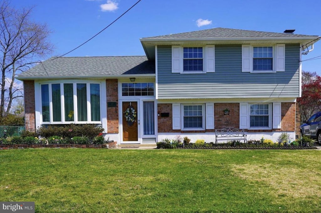 split level home featuring a shingled roof, a front yard, and brick siding