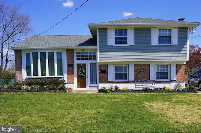 tri-level home with brick siding, roof with shingles, and a front lawn