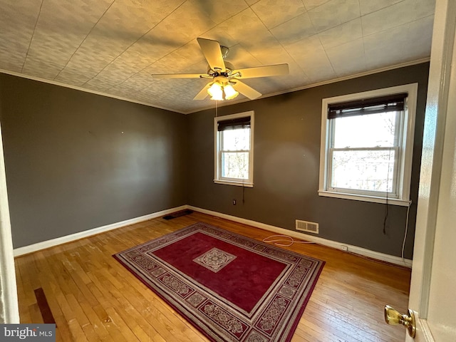 empty room with ceiling fan, hardwood / wood-style flooring, visible vents, baseboards, and ornamental molding