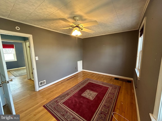 interior space with ornamental molding, wood finished floors, a ceiling fan, and baseboards