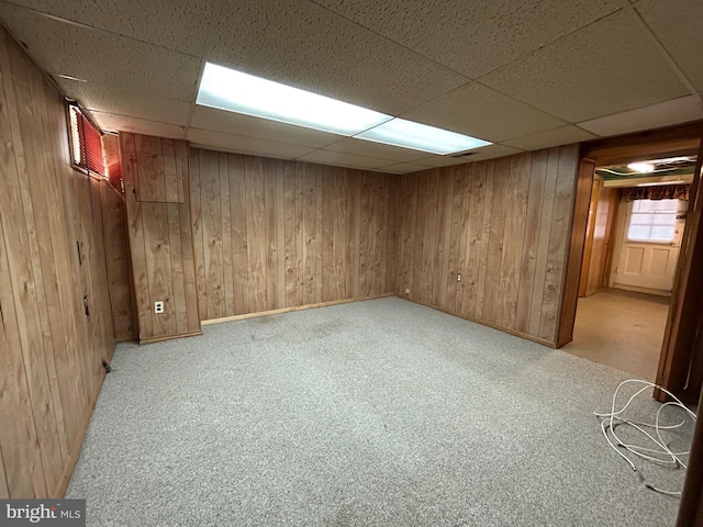 below grade area with a paneled ceiling, carpet, and wooden walls