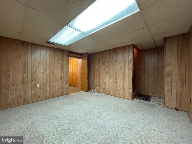 finished below grade area featuring a drop ceiling, wooden walls, and carpet flooring