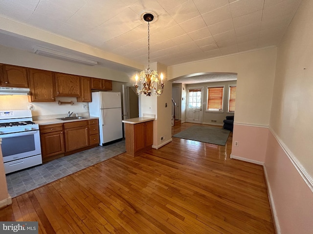 kitchen with under cabinet range hood, white appliances, a sink, light countertops, and brown cabinets