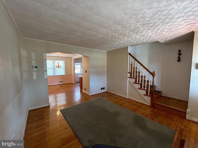 unfurnished living room featuring baseboards, stairs, arched walkways, and wood finished floors