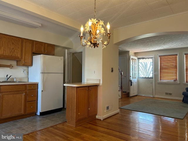 kitchen featuring dark wood finished floors, light countertops, brown cabinetry, freestanding refrigerator, and a sink