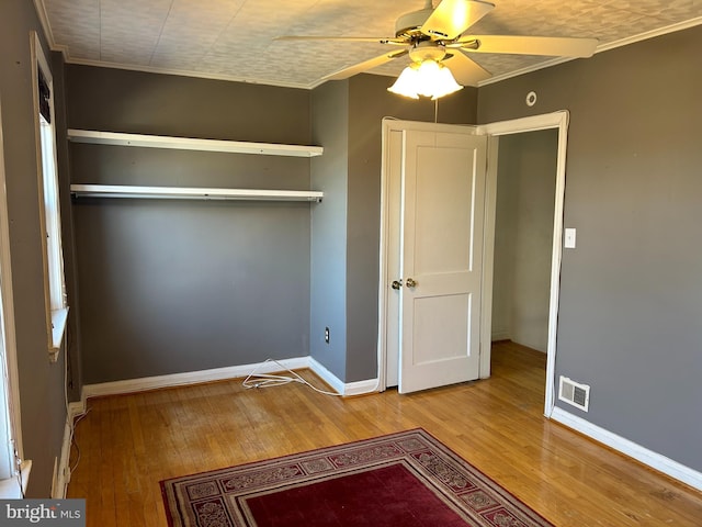 unfurnished bedroom featuring hardwood / wood-style flooring, baseboards, visible vents, and crown molding