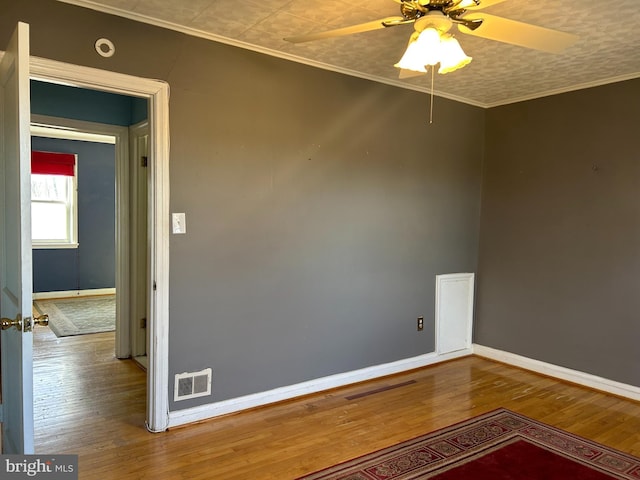 spare room featuring hardwood / wood-style floors, ornamental molding, visible vents, and baseboards