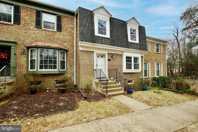 view of front of home with brick siding, mansard roof, and roof with shingles