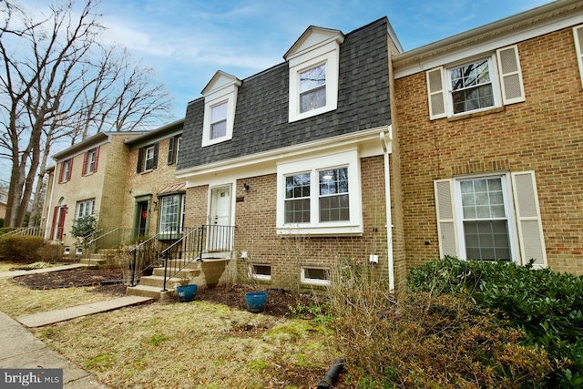 view of front of home with brick siding, mansard roof, and roof with shingles