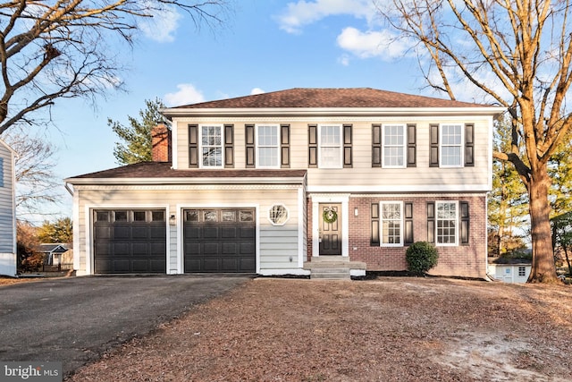 colonial inspired home featuring roof with shingles, aphalt driveway, and brick siding