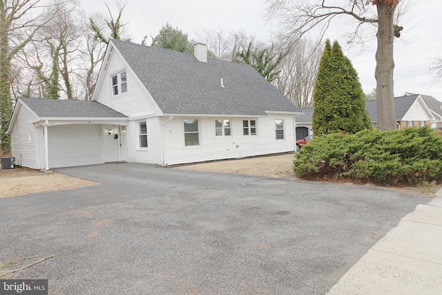 cape cod-style house featuring aphalt driveway, an attached garage, central AC, a shingled roof, and a chimney