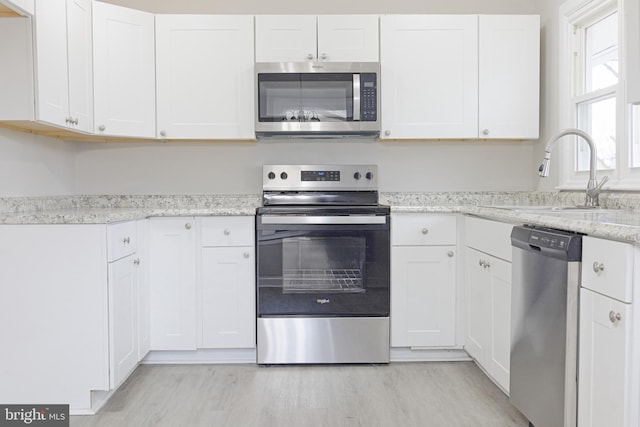 kitchen featuring light stone counters, stainless steel appliances, light wood-style flooring, white cabinetry, and a sink